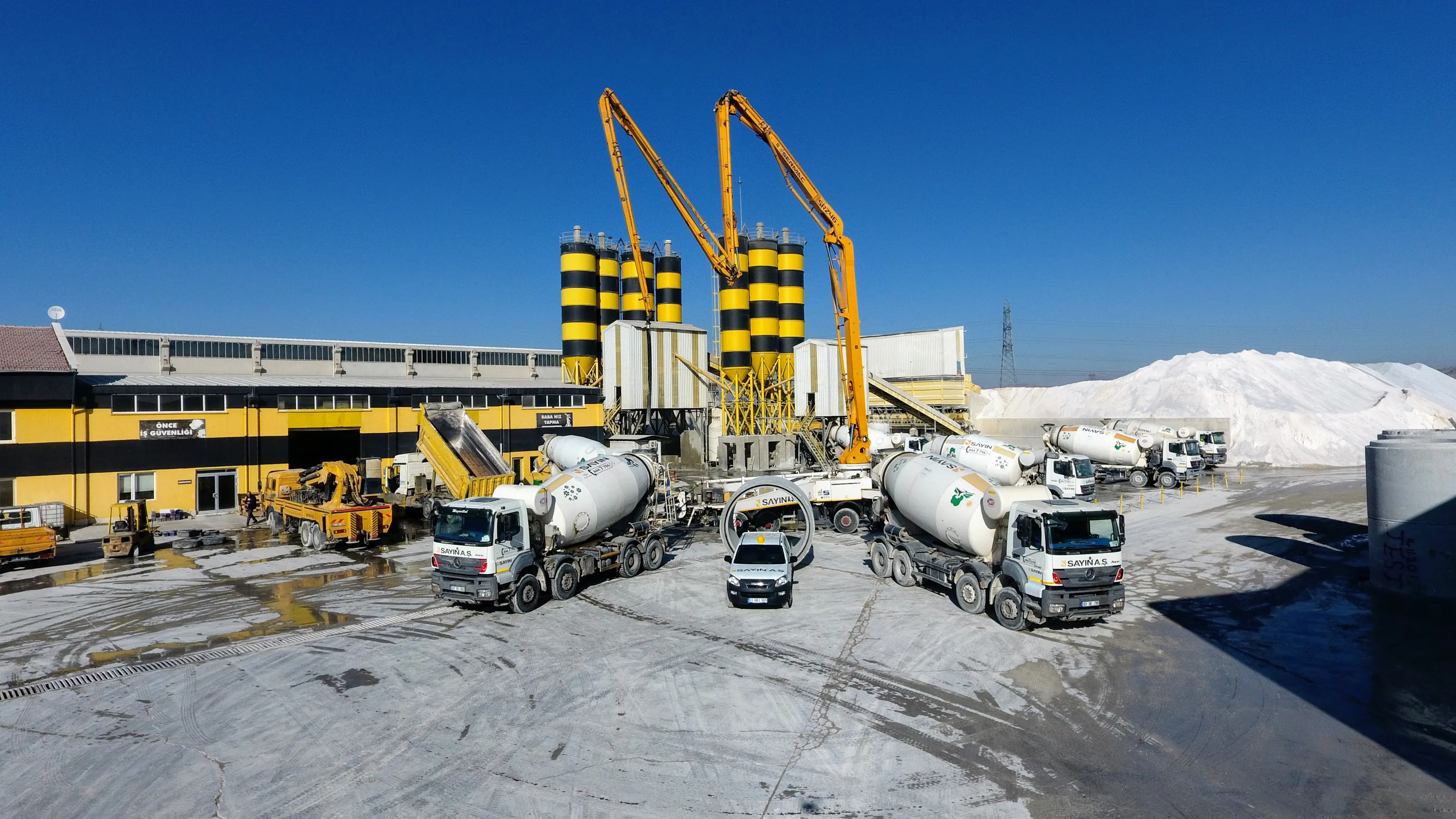Hazır beton santrali — sarı-siyah silolar, beton pompaları ve SAYIN mikserleri, havadan görünüm.